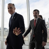 Mark Carney et Steven Guilbeault marchent devant des fenêtres qui montrent le centre-ville de Montréal.
