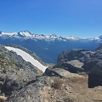 Derrière des rochers dénudés, on aperçoit des montagnes aux sommets enneigés.