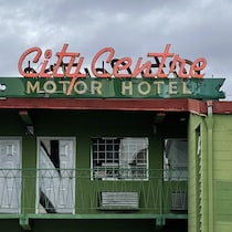 Façade d'un motel avec portes, fenêtres et balcons, surmontée d'une enseigne au néon sur laquelle est écrit City Centre Motor Hotel.