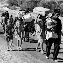 Un groupe de réfugiés palestiniens marche sur une route de terre. 