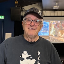 Un homme avec un chandail de Bob Dylan et une casquette des Beatles devant un écran avec des bas de Noël. 