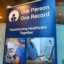 Une bannière bleue avec les mots «One Person One Record» et la photo de deux travailleurs de la santé en uniforme bleu, dont les visages sont camouflés.