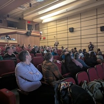 Des citoyens sont assis dans la salle et sont tournées vers une personne pose une question au micro.