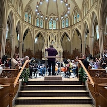 Le maestro Alain Trudel dirige les musiciens assis devant lui.