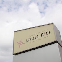 L'insigne de la Division scolaire Louis-Riel contre un ciel nuageux. 