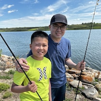Un jeune et et son père au bord d'un cours d'eau tiennent chacun une ligne le 13 juillet 2024 proche du lac Blackstrap.