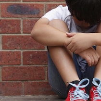 Un enfant triste contre un mur.