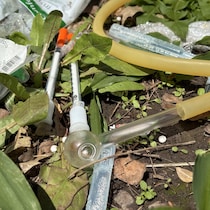 Une pipe de verre et des seringues sur le sol, dehors.