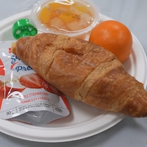 Une assiette qui contient un croissant, une orange, des fruits dans le sirop et une compote de fruits.