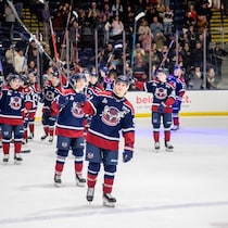 Une dizaine de joueurs en uniforme sont sur la glace après le match et lèvent leurs bâtons pour saluer les spectateurs, debout pour applaudir dans un aréna rempli.
