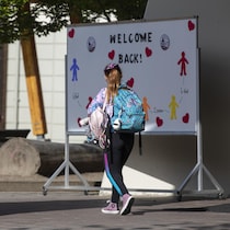 Jeune fille avec un sac sur le dos devant une affiche souhaitant un bon retour à l'école.