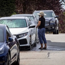 Une personne lave une voiture avec un tuyau d'arrosage.