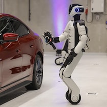 Un robot se tient devant une voiture rouge.