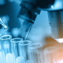 Un compte-goutte duquel est déversé un liquide dans des fioles posées devant un microscope.