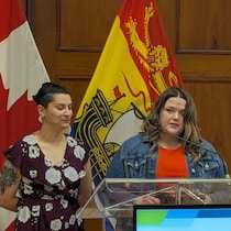 Daphnée Auclair et Kristen Barnes derrière un podium, des drapeaux du Canada et du Nouveau-Brunswick derrière elles.