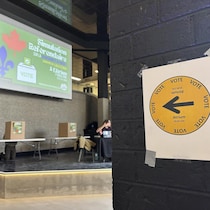 En premier plan, une affiche indiquant où aller voter. En deuxième plan, des urnes pour voter.