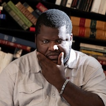 L'homme se tient le visage de manière pensive devant une bibliothèque remplie de livres.