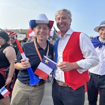 Tim Houston, vêtu d'une veste tricolore aux couleurs du drapeau acadien, et Colton LeBlanc, coiffé d'un chapeau aux couleurs du drapeau acadien, posent ensemble pour une photo dehors au milieu d'une foule.