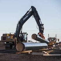 Un travailleur debout à côté d'une pelle mécanique qui soulève un tuyau de pipeline.