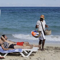 Des touristes prennent un bain de soleil tandis qu'un vendeur propose des cerfs-volants décorés du drapeau cubain.