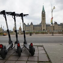 Trois trottinettes électrisques stationnées devant le Parlement à Ottawa en été.