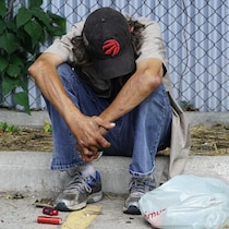 Une personne est assise sur un trottoir, la tête baissée, devant une clôture métallique.