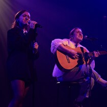 Deux artistes chantent, l'une des deux joue de la guitare.