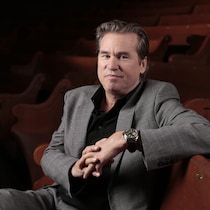 Val Kilmer est assis sur un banc en bois.