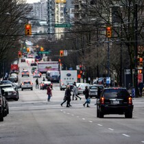 Plan large d'une rue avec des piétons qui traversent et les voitures stoppées à la lumière.