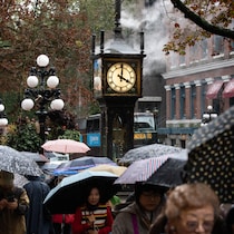 Des personnes portant des parapluies marchent devant une horloge à vapeur.
