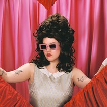 Portrait de la chanteuse avec des lunettes de soleil, tenant des rideaux rouges avec ses mains pour former un coeur.