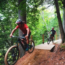 Deux sportifs sur des vélos de montagne qui se suivent sur un chemin forestier.