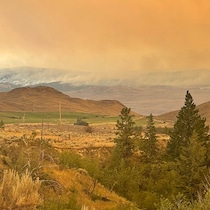 À l'arrière-plan, de la fumée s'échappe d'une montagne, couvrant le ciel d'un voile de couleur orange.