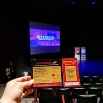 Une personne tient un billet pour la Compétition des courts métrages canadiens-français devant le grand écran du Salon Pauline Boutal.