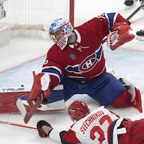 Il étire la jambière pour bloquer un tir d'un adversaire qui est étendu sur la glace.