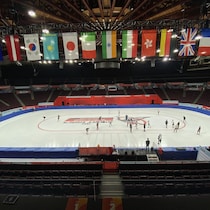 Vue d'ensemble d'un aréna avec des patineurs sur la glace et des drapeaux suspendus au plafond