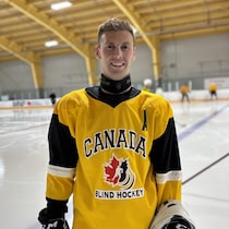 Simon est debout, sur la glace, souriant, et portant son gilet du Canada avec l'inscription Blind hockey.