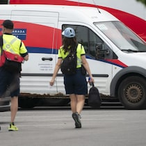 Deux employés de Postes Canada marchent dans un stationnement de la société d’État.