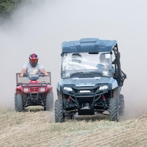 Deux VTT conduits par des gens portant des casques circulent à travers un champ agricole en faisant de la fumée et de la poussière.