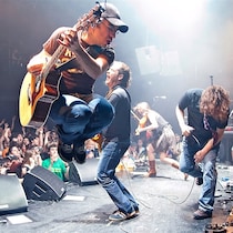 Un guitariste saute dans les airs devant une foule en liesse.