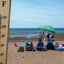 Vue rapprochée d'un thermomètre indiquant 31 degrés Celsius et en arrière-plan des gens sur une plage.
