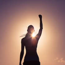 Une femme a le poing levé en regardant le soleil en signe de victoire.