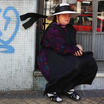 Une mennonite assise devant la vitrine d'un commerce, à côté d'un graffiti bleu illisible, regarde la caméra.