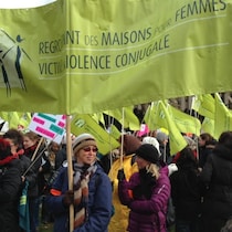 Dans une manifestation, des femmes tiennent des affiches, majoritairement du Regroupement des maisons pour femme victimes de violence conjugale.