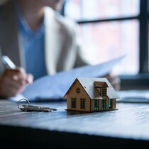 Clés et maison sur la table devant un individu signant des papiers.