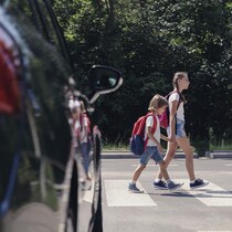 Deux enfants traversent un passage piéton avec une voiture qu'on voit au premier plan.