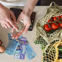 Une femme compte de l'argent dans sa main. Des oeufs et des légumes sont posés sur la table.