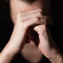 Une femme dont le visage est caché par ses mains en premier plan, paume droite sur poing gauche.
