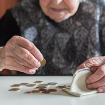 Une dame âgée compte ses sous, posés sur une table devant elle. 
