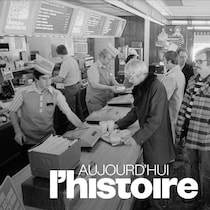 La clientèle fait la file au MacDonald's et le personnel s'affaire derrière le comptoir dans une photo en noir et blanc. 